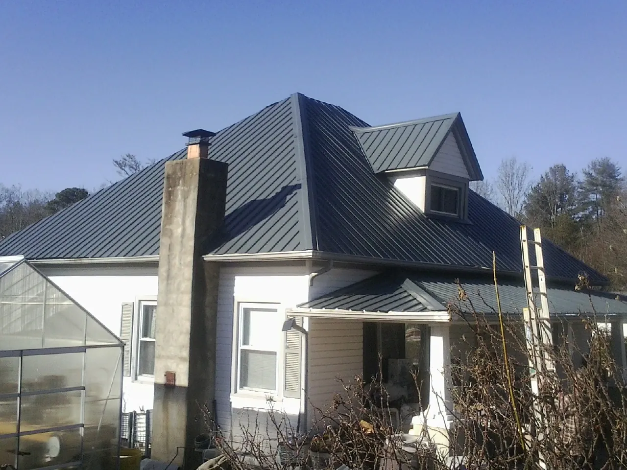 Dark blue standing seam metal roof on a white farmhouse with dormer — Slate & Tile Roof Repair by Roofing Brothers in Newville