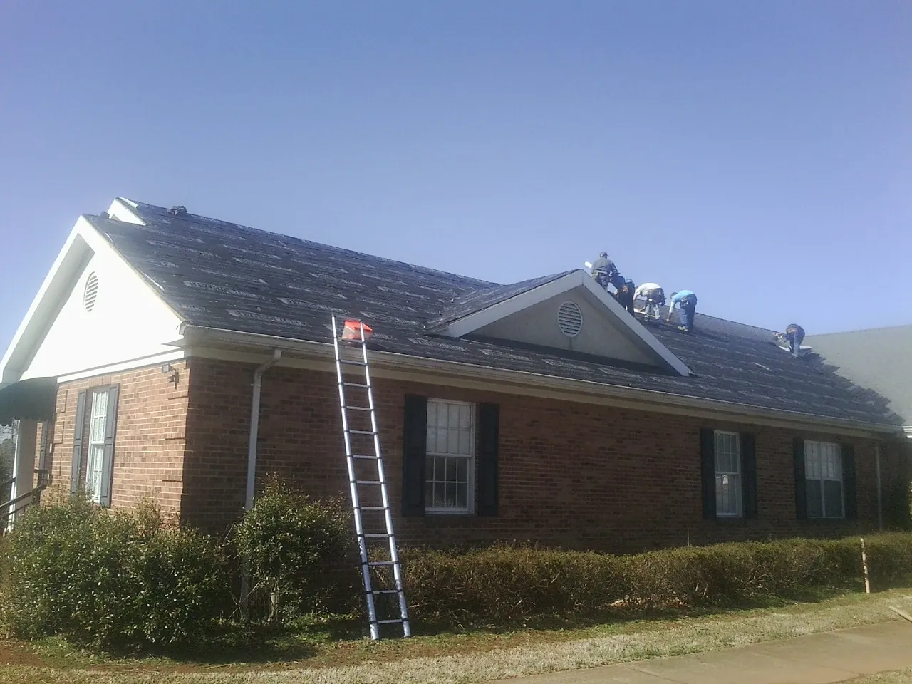 Crew tearing shingles off a brick ranch roof with a ladder set — Emergency Roof Repair work by our crew in Newville