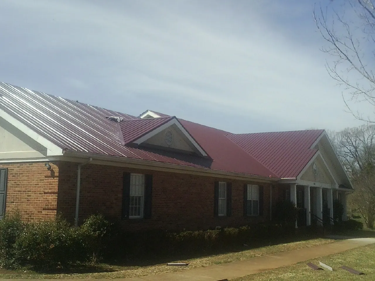 Red metal roof with gabled entries on a long brick building, from a Hail Damage Roof Repair job in Newville