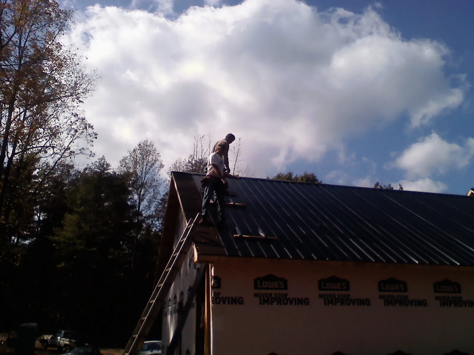 Roofer fastening dark metal panels high against a cloudy sky, from a Roof Inspection job in Newville
