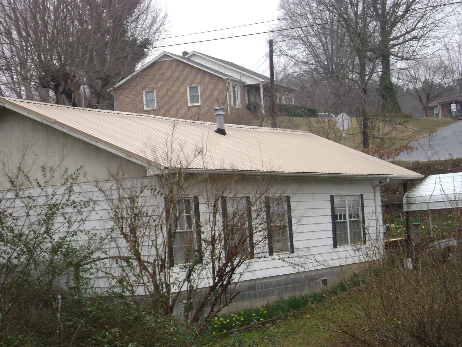 Tan metal roof on a white sided house set into a hillside — Commercial Roofing by Roofing Brothers in Newville